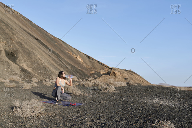 Fit young woman in sportswear drinking water after a workout session outside in extreme terrain