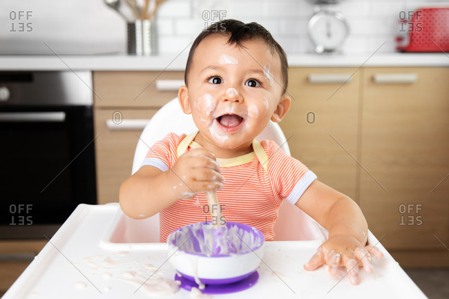 Happy baby in high chair eating yogurt with messy face