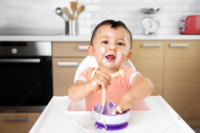 Cute baby with messy face eating yogurt