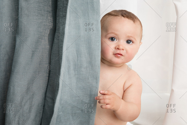 Cute baby face peeking behind curtains at home