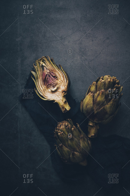 Whole and cut artichokes on dark surface viewed from above