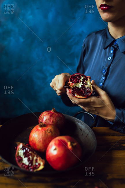 A woman wearing red lipstick cutting pomegranate fruits in front of blue background