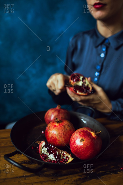 Woman wearing red lipstick cutting pomegranate fruits in kitchen