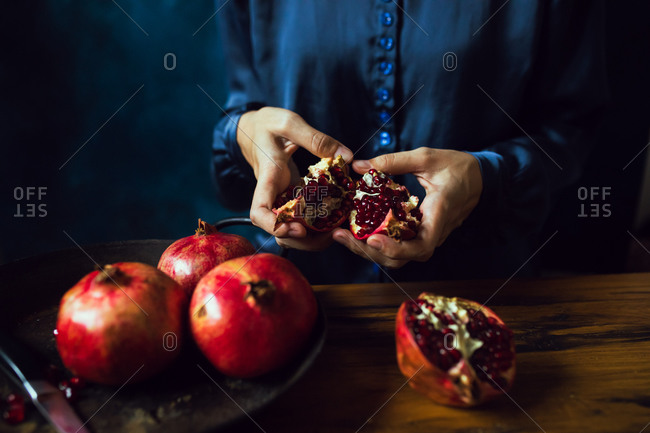 Close up of a woman's hands breaking opening a pomegranate fruit in kitchen