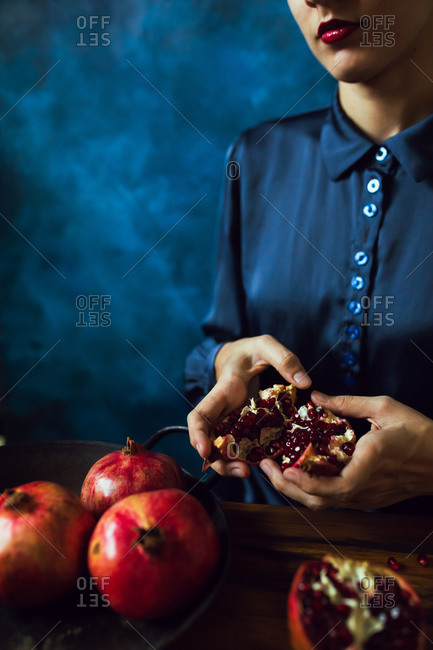 A woman's breaking opening a pomegranate fruit in kitchen