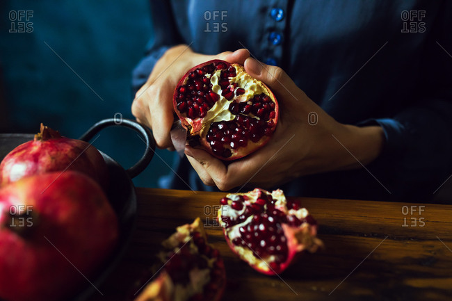 Woman using knife to cut pomegranate fruits in kitchen