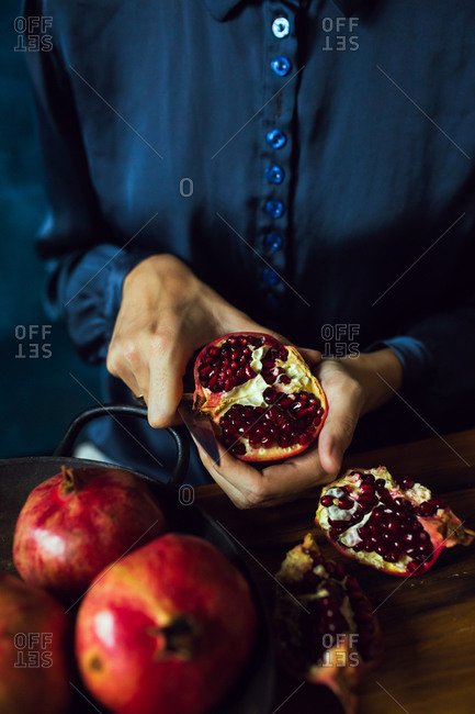 Close up of a woman using knife to cut pomegranate fruits in kitchen