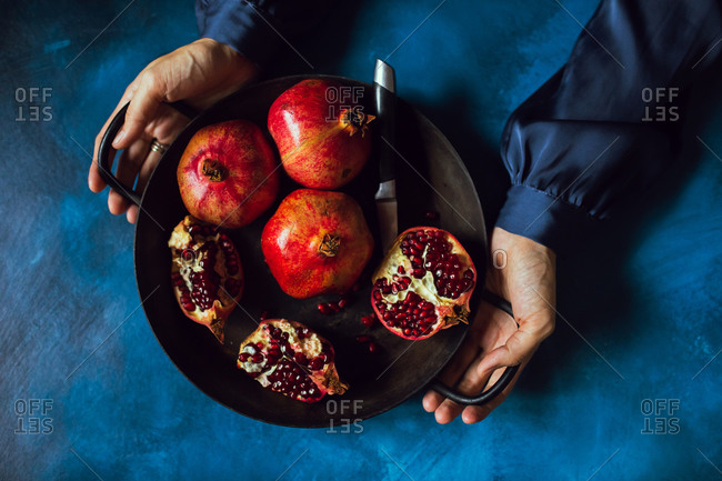 Overhead view of a woman holding bowl filled with pomegranate fruits
