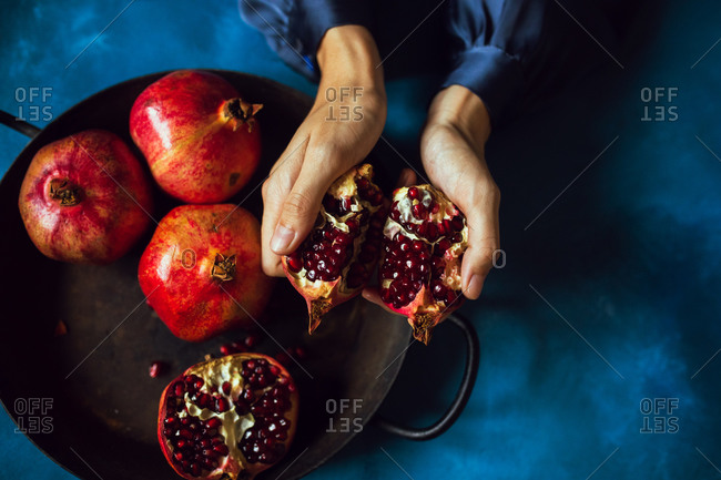 Woman's hands breaking opening a pomegranate fruit viewed from above