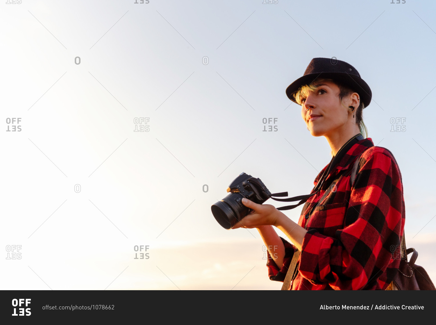 Side view of androgynous female traveler with professional photo camera standing on hill in mountainous area