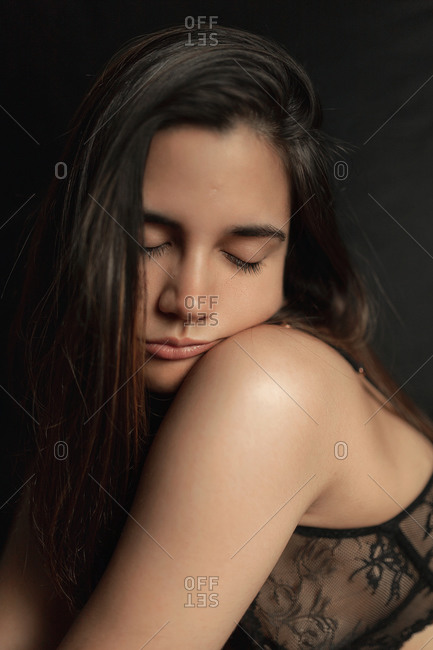 Serene slim female in black lace bra with eyes closed on dark background in studio