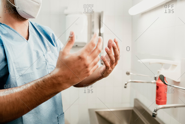 Side view of crop unrecognizable surgeon washing hands over sink while preparing for medical procedure in hospital