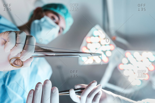 From below side view of focused professional surgeon with medical scissors working in operating room in modern hospital