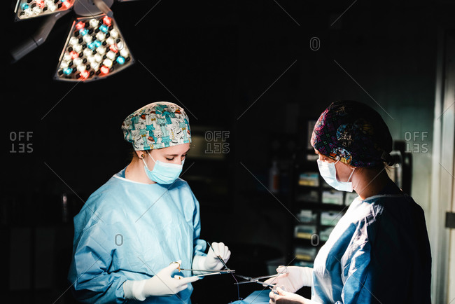 Side view of focused professional surgeons with surgical tools and thread finishing operation of patient in operating theater