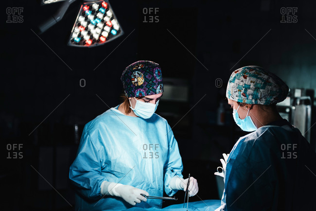 Side view of focused professional surgeons with surgical tools and thread finishing operation of patient in operating theater