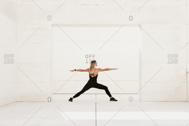Full body side view of slim female in black sportswear performing balancing Warrior asana while practicing yoga in spacious light studio
