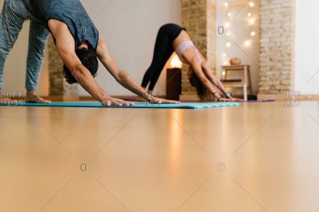 Unrecognizable people doing Downward Facing Dog pose with outstretched arms during group yoga lesson
