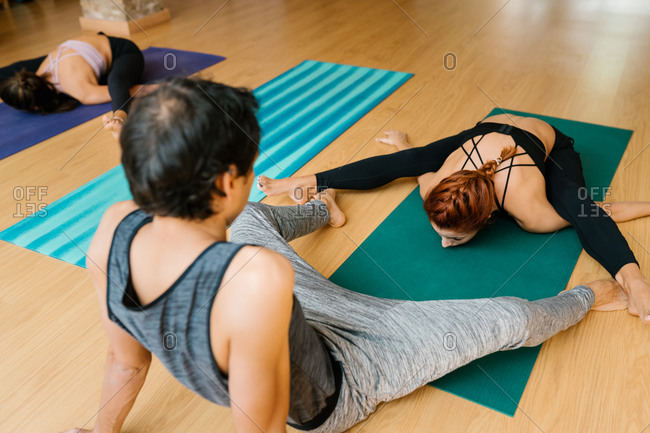 High angle of slim female doing Upavista Konasana pose near male coach and stretching body during group yoga lesson in studio