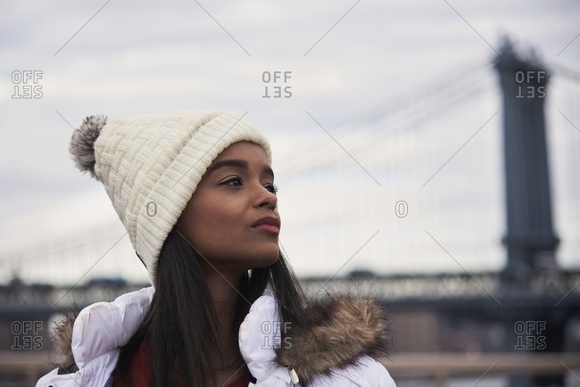 Tranquil African American female in warm outerwear near metal bridge and looking away during stroll in New York city