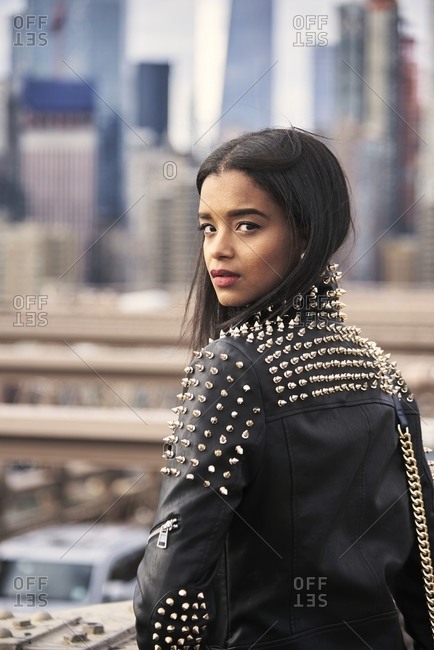 Back view of thoughtful African American female in leather jacket sitting on street in New York and enjoying cityscape