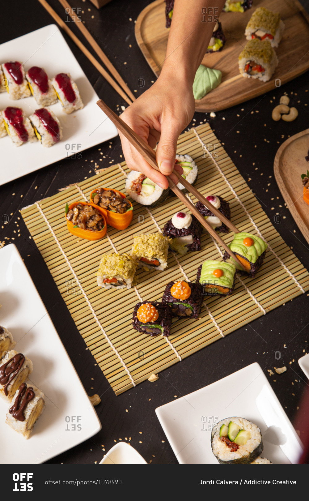 From above of crop unrecognizable hand with chopsticks taking assorted veggie sushi from bamboo mat