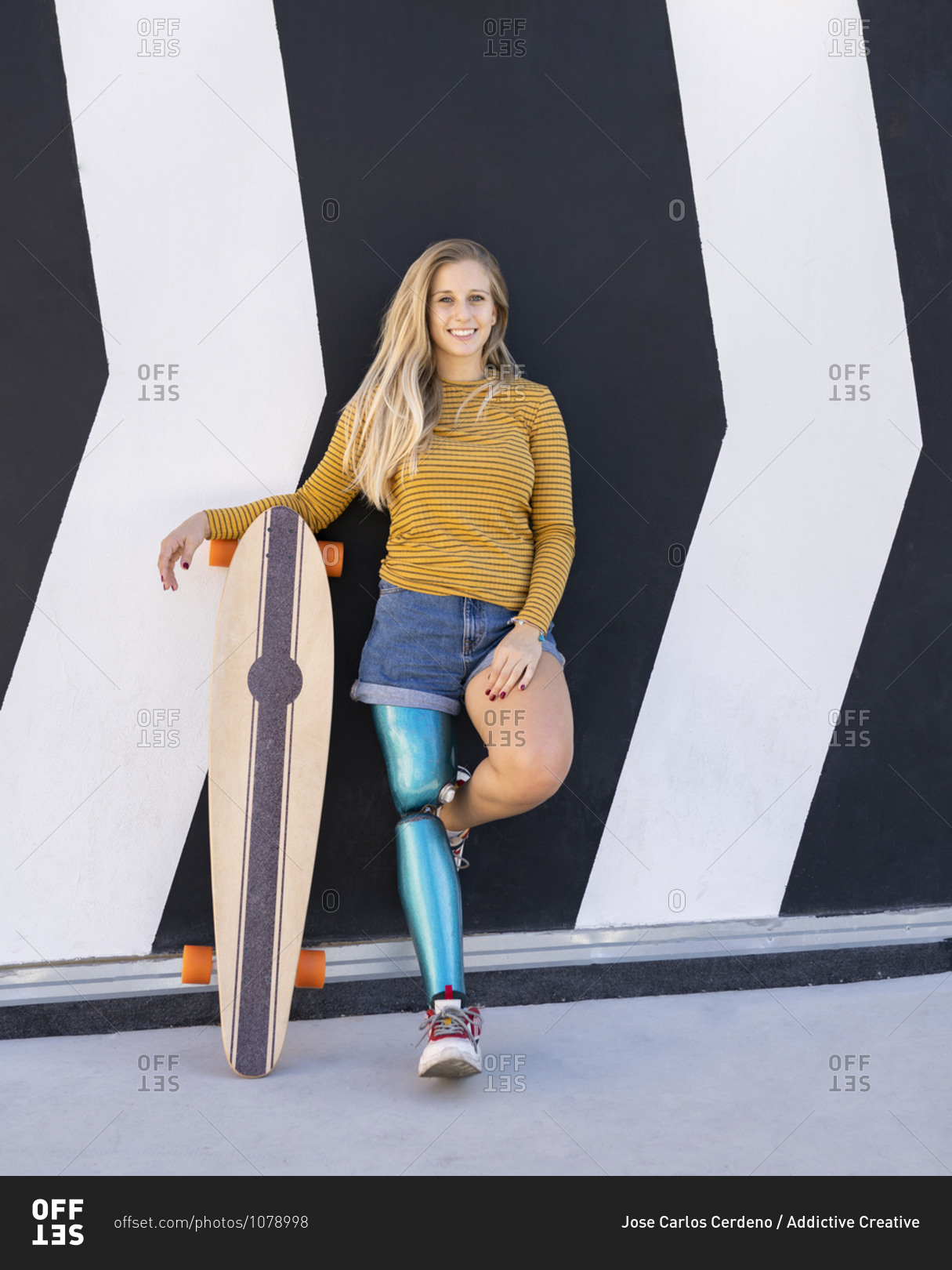 Delighted female skater with bionic prosthesis of leg standing near building in street and looking at camera