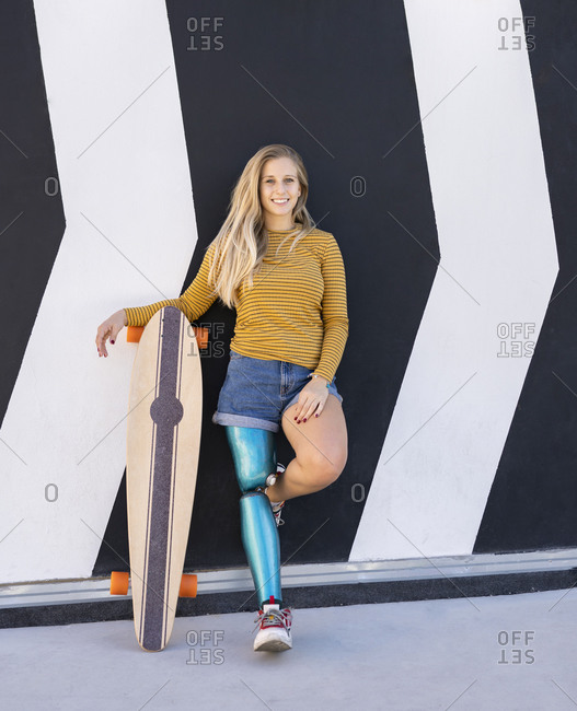 Delighted female skater with bionic prosthesis of leg standing near building in street and looking at camera