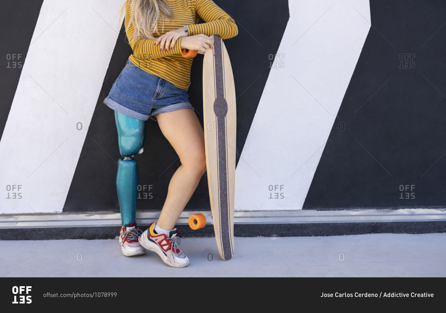 Unrecognizable female skater with bionic prosthesis of leg standing near building in street