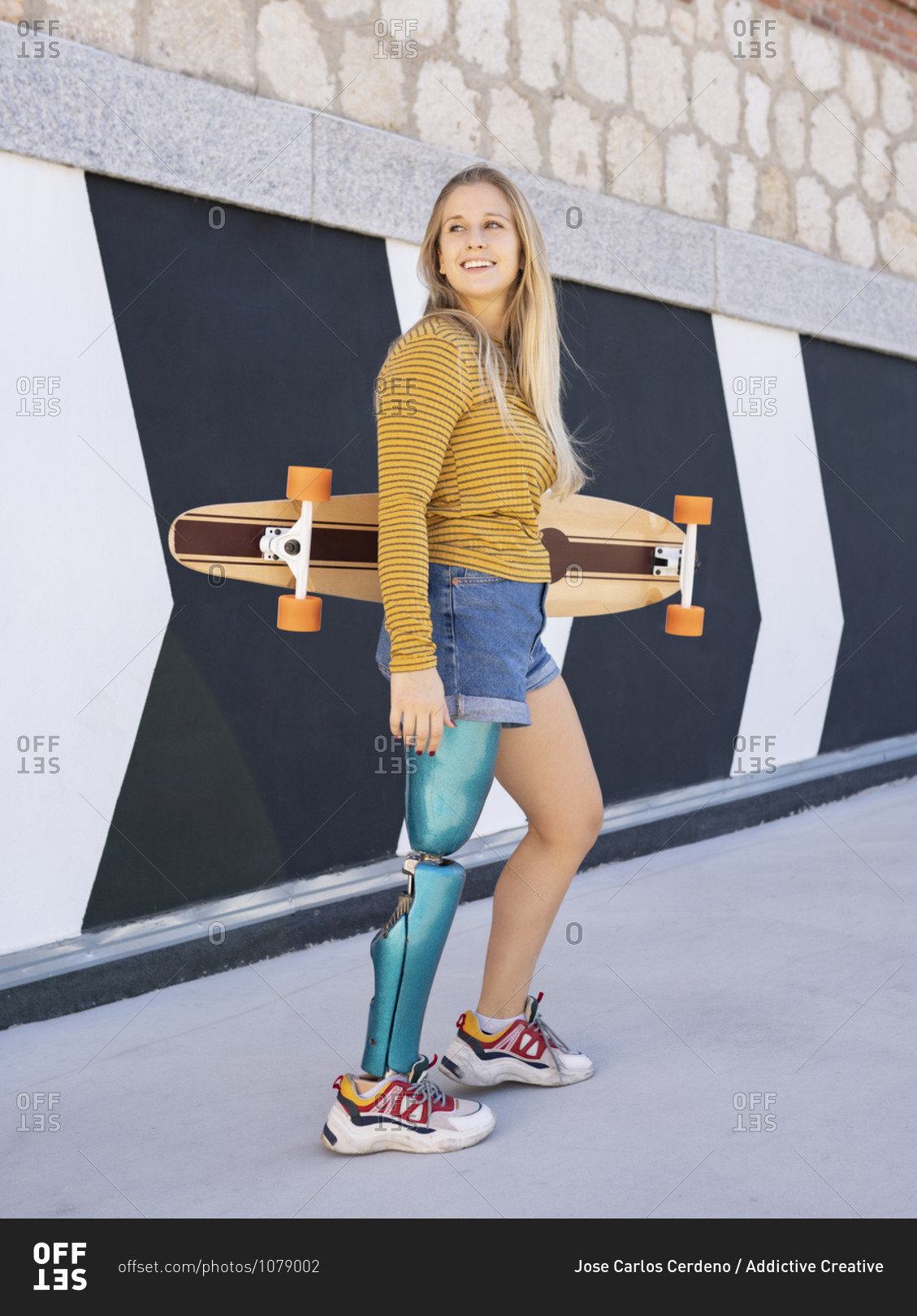 Delighted female skater with bionic prosthesis of leg standing near building in street and looking away