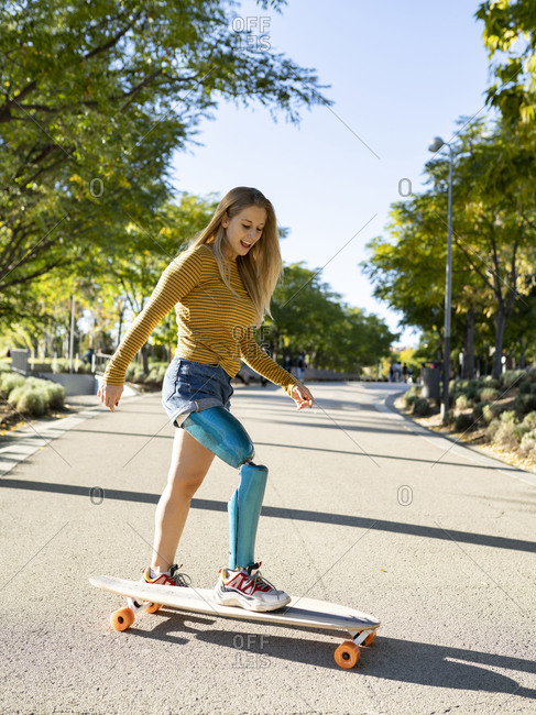 Side view of positive female with leg artificial limb of leg riding longboard on road in summer