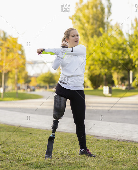 Focused Paralympic female runner with leg prosthesis stretching body and doing forward bend during training