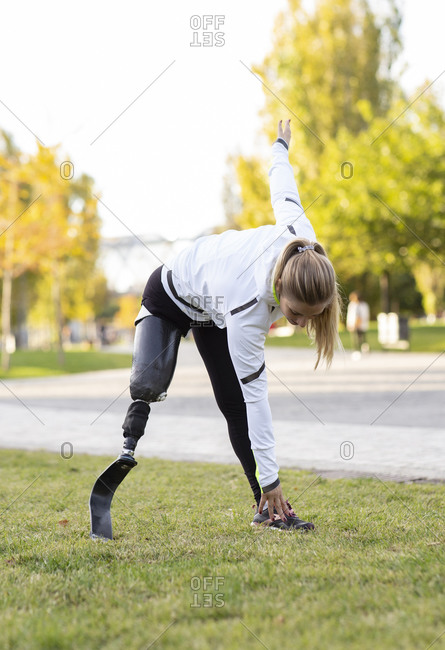 Focused Paralympic female runner with leg prosthesis stretching body and doing forward bend during training