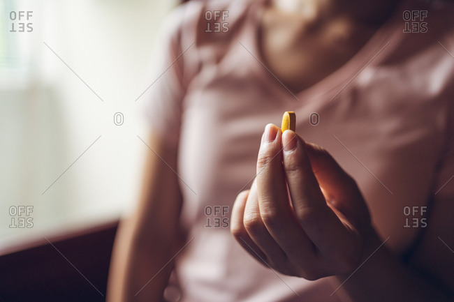 Crop unrecognizable healthy female showing bright yellow vitamin pill during health care routine at home