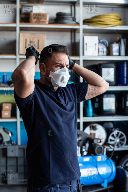 Male employee putting white face mask for work in garage