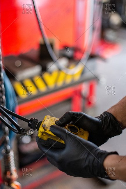 Side view of crop hands of anonymous mechanic in protective gloves using special tool for control and diagnostic of machine engine while working in workshop