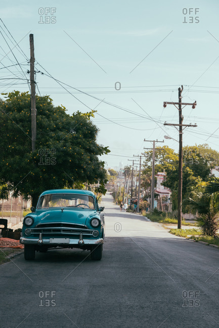 August 6, 2019: Blue retro automobile parked on narrow empty asphalt road on street of town in Cuba