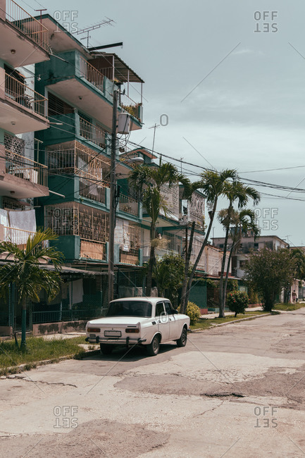 August 6, 2019: Exterior of typical old residential building with car parked on roadside near uneven damaged road in urban area in Cuba