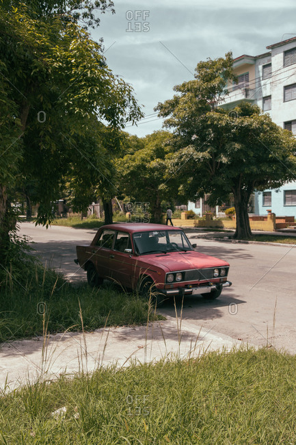 August 6, 2019: Exterior of typical old residential building with car parked on roadside near uneven damaged road in urban area in Cuba
