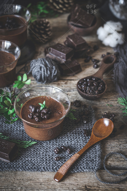 Tasty chocolate mousse in glass bowl arranged on wooden table with various ingredients