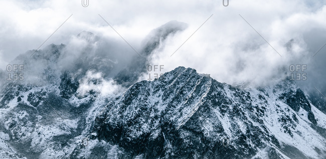 Majestic panoramic scenery of rough rocky slopes of mountain range covered with snow under cloudy sky