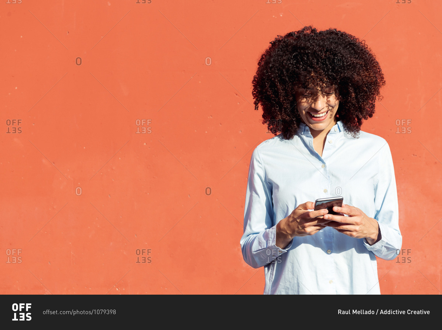 Content ethnic female entrepreneur in formal shirt texting on smartphone while standing in city on orange background