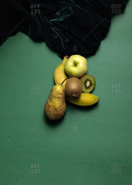 From above composition of fresh natural green pear and apple with kiwi and banana arranged on green background