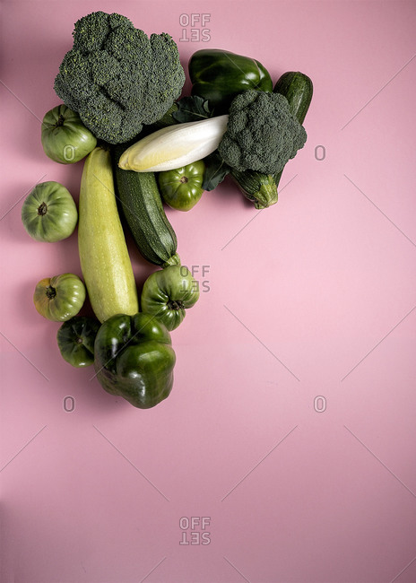 From above composition of green broccoli and peppers with tomatoes and zucchini arranged on pink background