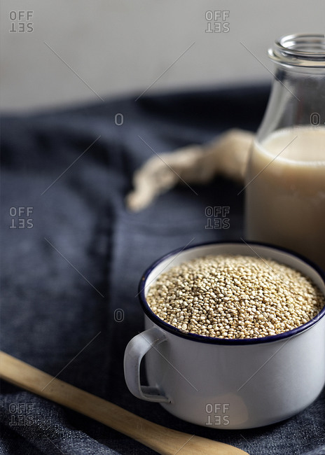Metal mug full of sesame seeds arranged on table with glass bottle of milk