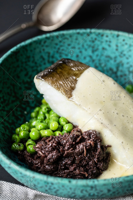 High angle closeup of delicious cod fish with green peas and cream sauce in bowl served on table in restaurant