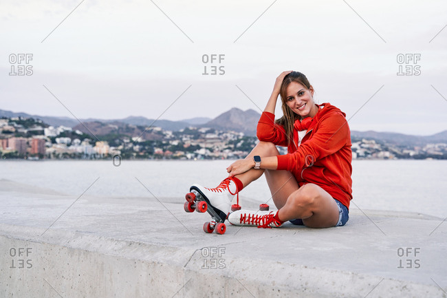 Peaceful female sitting resting on embankment in red and white roller skates looking at camera
