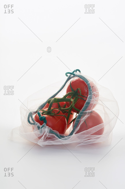 Still life with tomatoes in net mesh bag back lit on white background