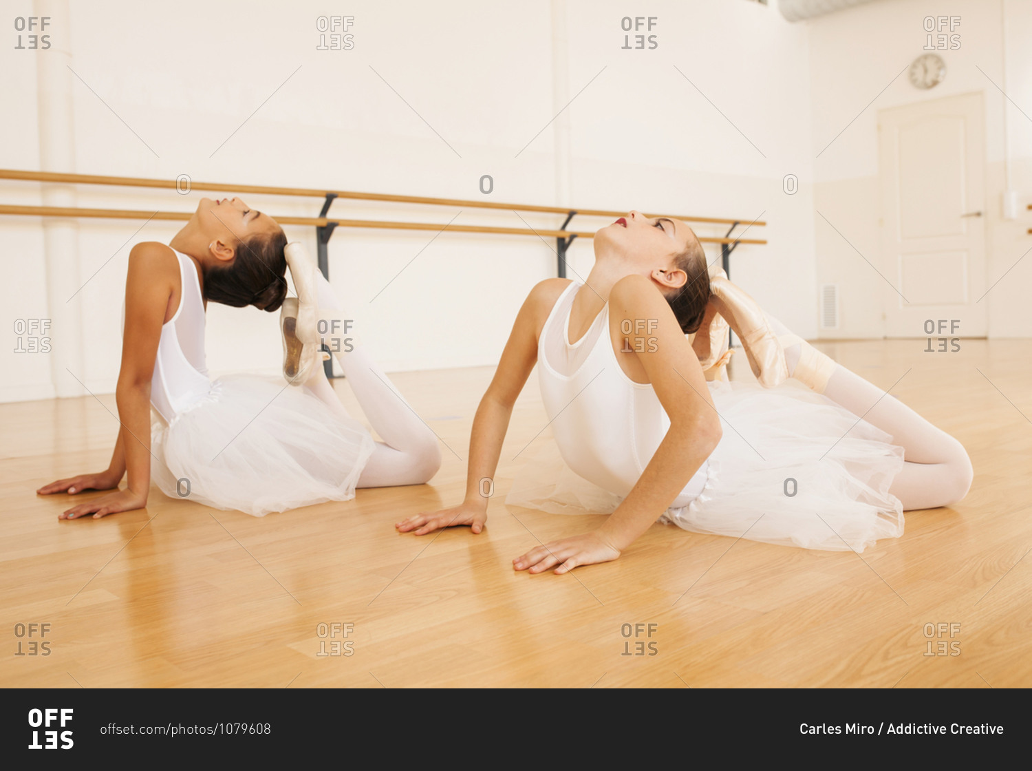 Side view of teenage ballet dancers in tutu and pointe shoes stretching body during lesson in dance hall looking up