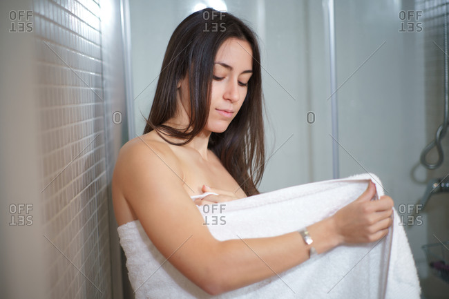 Side view of delicate female wrapping in white soft towel after taking shower while standing in bathroom and doing daily hygiene routine