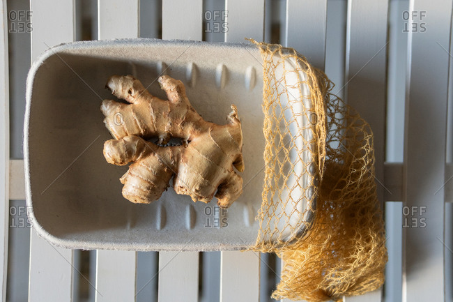 Top view of fresh ginger roots in paper container placed on wooden table on sunny day